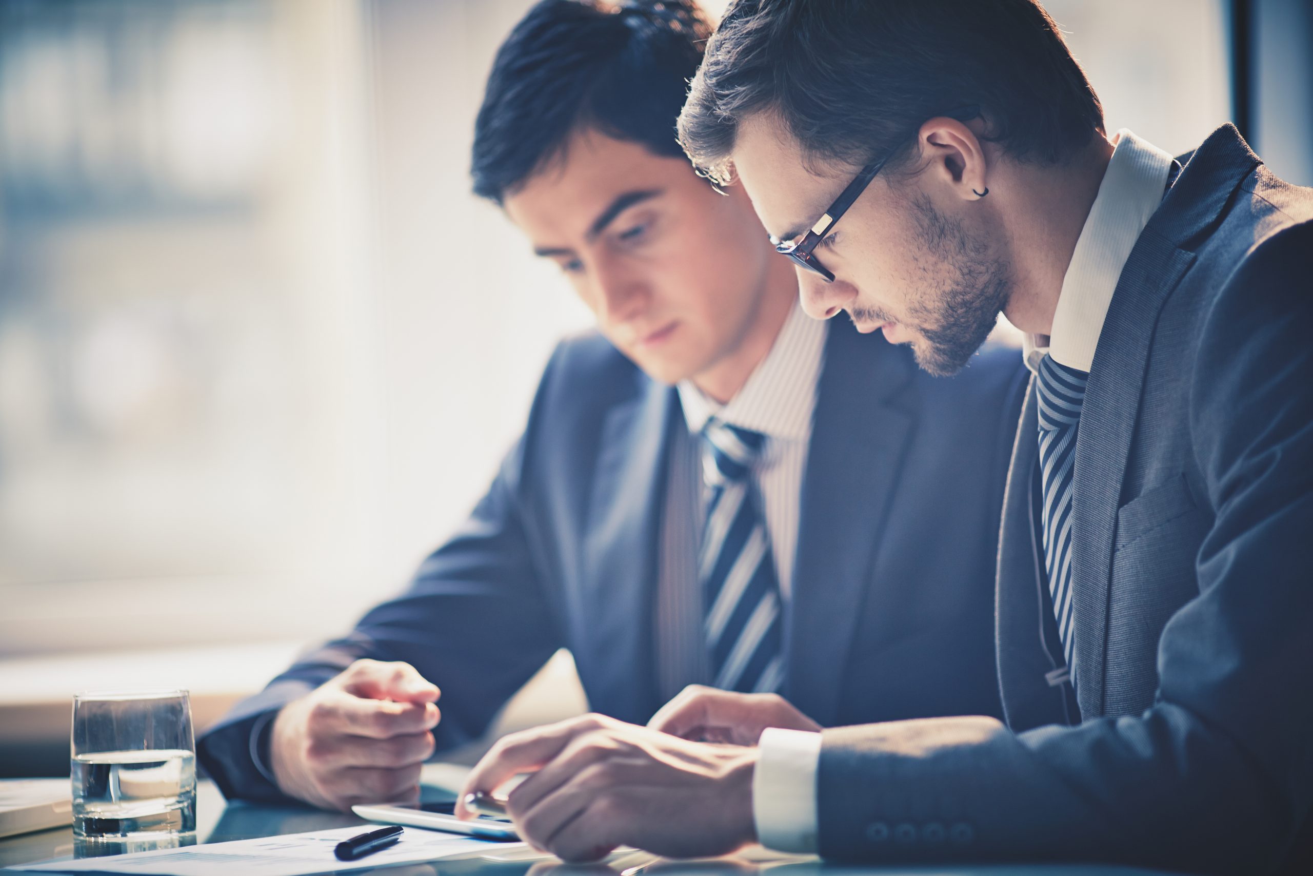 Image of two young businessmen using touchpad at meeting